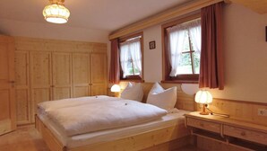 A wooden bedroom with a large bed, two bedside lamps, and a wooden dresser.