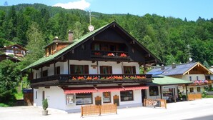A two-story building with a balcony, surrounded by lush greenery and a mountain backdrop.