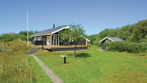 Eine moderne Hütte mit überdachter Terrasse, einem kleinen Garten und blauem Himmel.