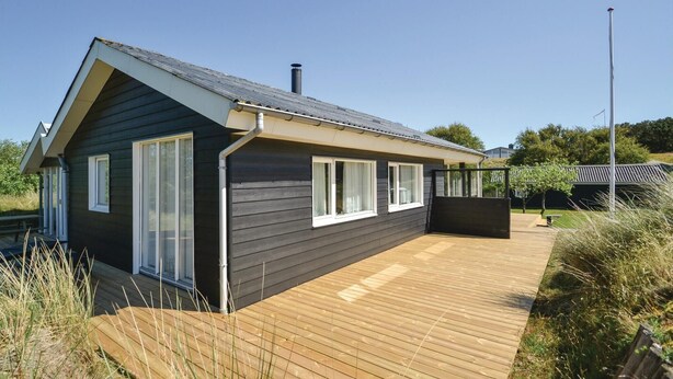 Eine moderne Hütte mit geneigtem Dach, großen Fenstern und einer Holzterrasse.