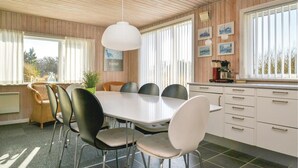 Ein Essbereich mit einem weißen Tisch und Stühlen, Holzwandverkleidung und einem Fenster mit Jalousien.