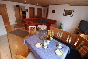 Un salón acogedor con un sofá rojo, una mesa de comedor con platos y tazas, y un televisor sobre un mueble de madera.