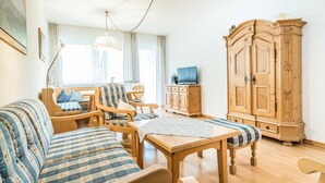 Una sala acogedora con un sofá, sillas, un aparador de madera y un televisor.