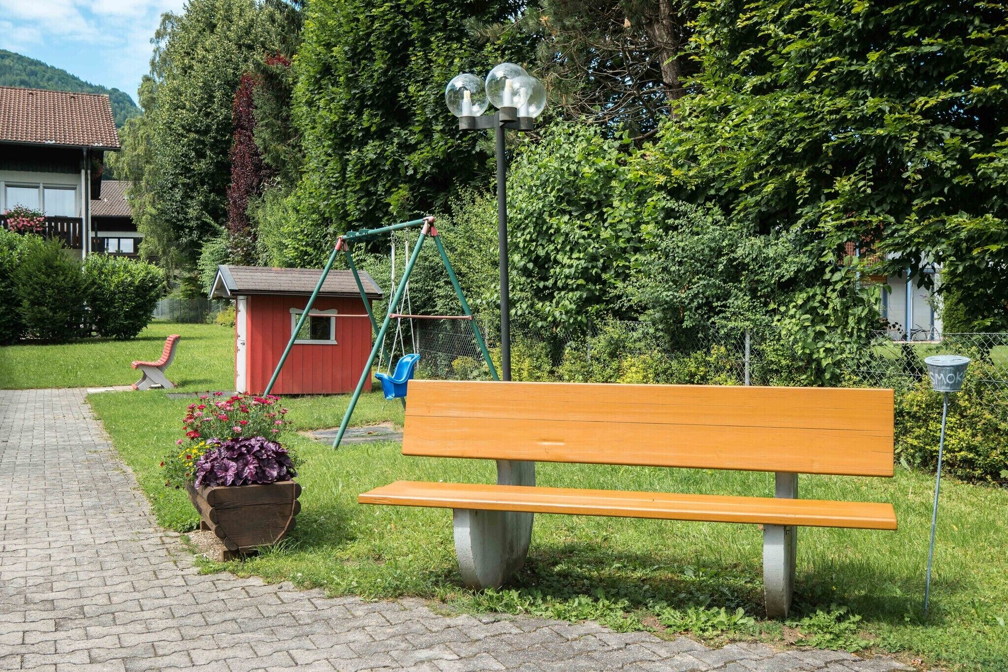 Un banc de parc, une balançoire et un petit abri dans un espace vert agrémenté d’un chemin pavé.