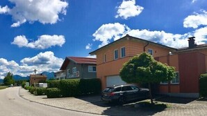Rua residencial com casas, um carro estacionado e céu azul.