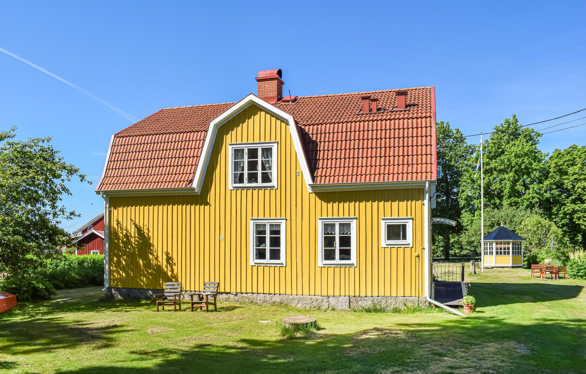 Ein gelbes Haus mit rotem Ziegeldach, einem Schornstein und einer kleinen Veranda mit zwei Stühlen.