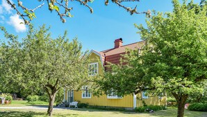 A yellow house with a red roof, surrounded by green trees and a well-maintained lawn. - Nice home in Växjö with kitchen (Växjö)