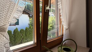 A room with a window overlooking a forested area, a green kettle on the windowsill, and a wooden door with a handle. - Apartment no. 4 Amara for 1-3 pers., 42 m², 1 sep. bedroom. (Bischofswiesen)