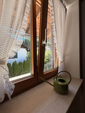 A room with a window overlooking a forested area, a green kettle on the windowsill, and a wooden door with a handle. - Apartment no. 4 Amara for 1-3 pers., 42 m², 1 sep. bedroom. (Bischofswiesen)