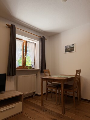 A room with a dining table, chairs, a radiator, a window with curtains, a picture on the wall, and a TV on a stand. - Apartment no. 4 Amara for 1-3 pers., 42 m², 1 sep. bedroom. (Bischofswiesen)