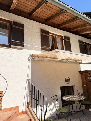 A building with a wooden balcony, a small table with chairs, and a sign above the entrance. - Apartment no. 4 Amara for 1-3 pers., 42 m², 1 sep. bedroom. (Bischofswiesen)