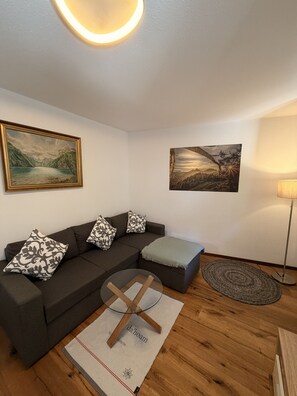 A modern living room with a dark brown sofa, patterned cushions, two wall-mounted paintings, a standing lamp, and a wooden floor. - Apartment no. 4 Amara for 1-3 pers., 42 m², 1 sep. bedroom. (Bischofswiesen)