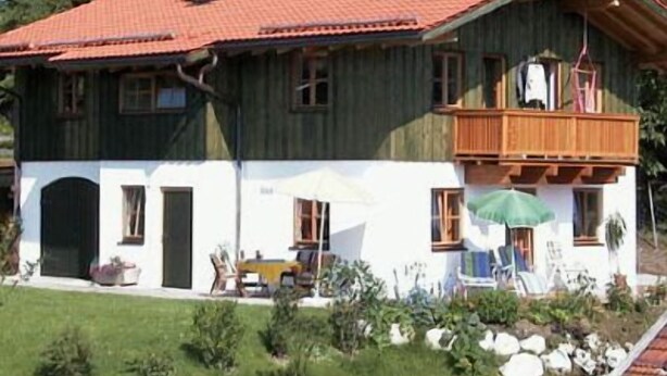 Una casa a due piani con tetto in tegole rosse, un balcone e un piccolo giardino con piante e un tavolo.