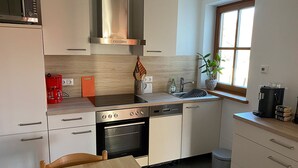 Una cucina moderna con mobili bianchi, una cappa in acciaio inossidabile, forno integrato, lavastoviglie e una finestra che lascia entrare la luce naturale.