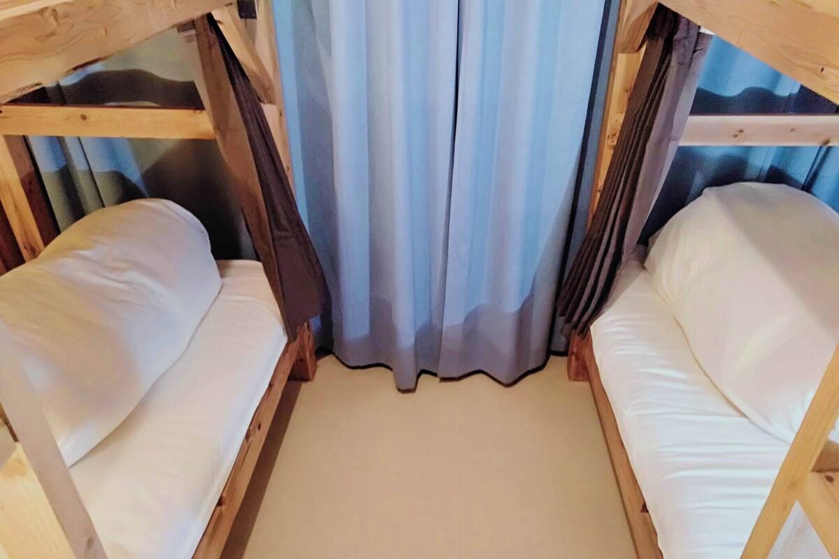 Une chambre avec un lit superposé, dont la structure est en bois, avec une literie blanche et un rideau.
