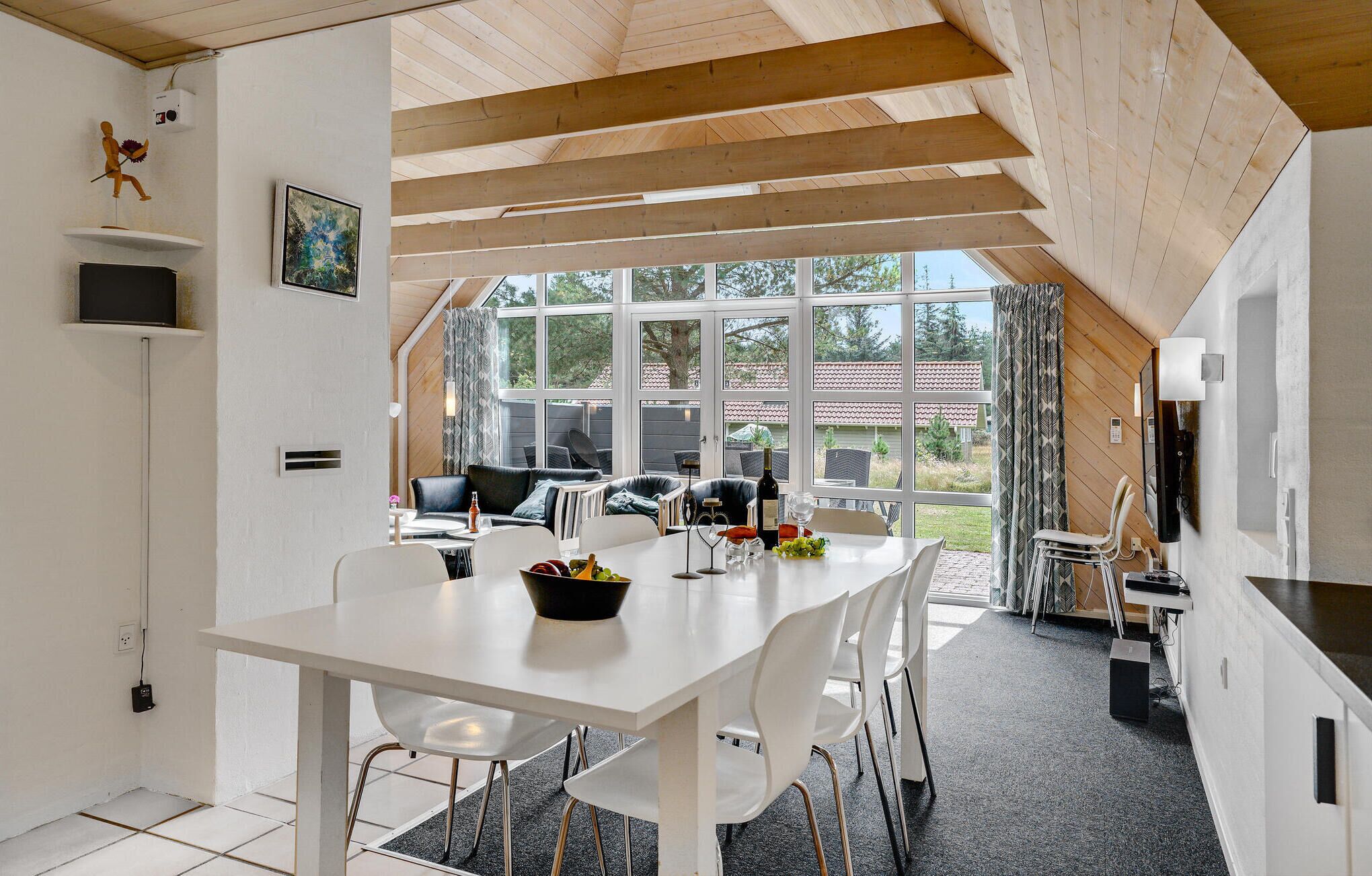 Une cuisine moderne avec des meubles blancs, un coin repas doté d’une table et de chaises blanches, et de grandes fenêtres offrant une vue sur l’extérieur.