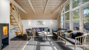 Ein gemütliches Wohnzimmer mit Kamin, einer Couch, Sesseln und großen Fenstern.