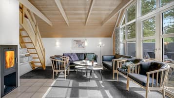 Un salon chaleureux avec une cheminée, un canapé, des fauteuils et de grandes fenêtres.
