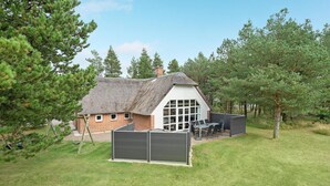 Ein reetgedecktes Cottage mit großem Fenster und einer Terrasse mit Sitzgelegenheit.