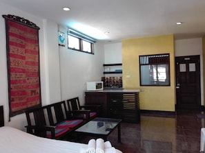 A hotel room with a bed, a sofa, a small dining table, a microwave, and a window with blinds.