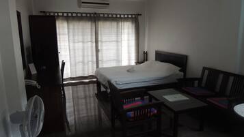 Een hotelkamer met een bed, een bureau, een stoel, een tafel, een ventilator en een raam met gordijnen.