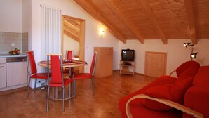 Eine moderne Küche mit Essbereich, Fernseher und einem roten Sofa.
