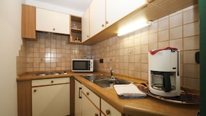 Eine Küche mit Holzschränken, einer Mikrowelle, einer Kaffeemaschine und einem Spülbecken.