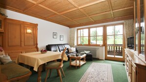 Ein gemütliches Wohnzimmer mit Holzbalkendecke, einem Esstisch, einer Couch und einem Fernseher.