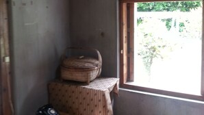 Une petite pièce rustique avec un plafond et des murs en bois, une seule fenêtre donnant sur la verdure, une table en bois avec une chaise, et un petit tabouret sur lequel se trouve un téléphone.