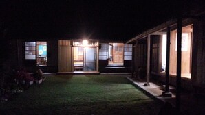 Une maison traditionnelle de style japonais, illuminée la nuit, avec une entrée bien éclairée et un petit jardin.