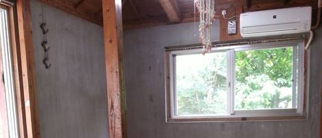 A room with tatami mats, a wooden ceiling, a window with a view of trees, and an air conditioning unit.