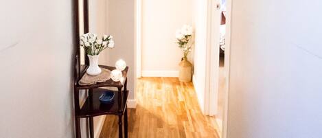 A hallway with wooden flooring, a mirror, framed pictures, and a vase with flowers.