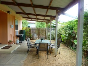 An outdoor patio with a table and chairs, surrounded by a wooden fence and lush greenery. - Rubys Cottage (Penola)
