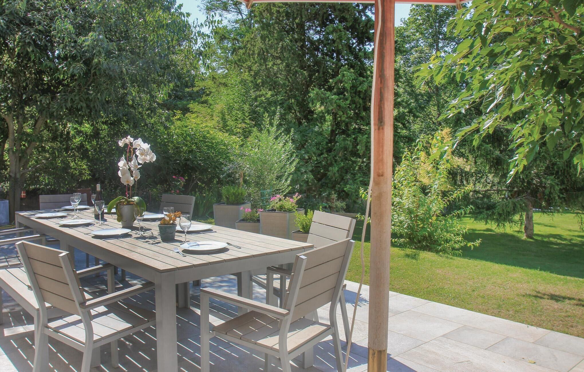 An outdoor dining area with a wooden table and chairs, surrounded by lush greenery and trees.