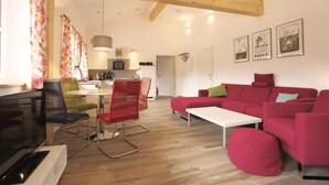 Un salon moderne avec un canapé rouge, une table basse blanche et un coin repas doté de chaises colorées.