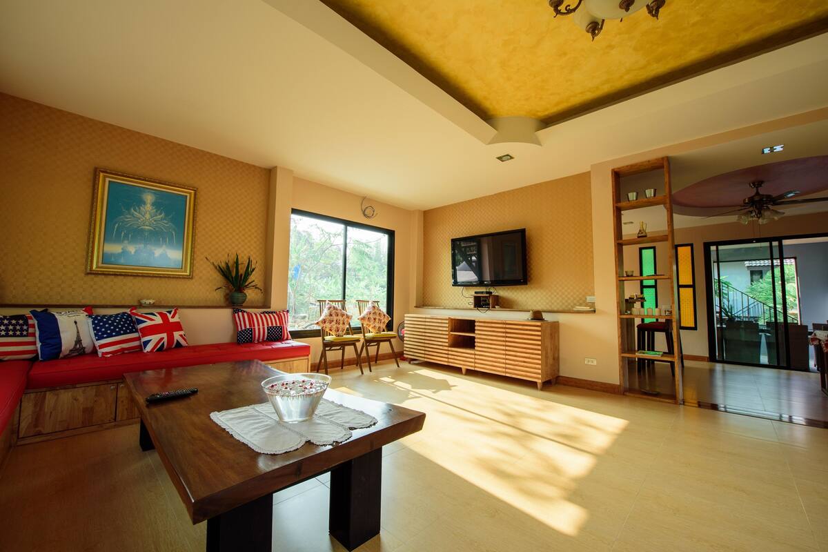 A spacious living room with a red sofa, a wooden coffee table, and a television on a wooden cabinet.