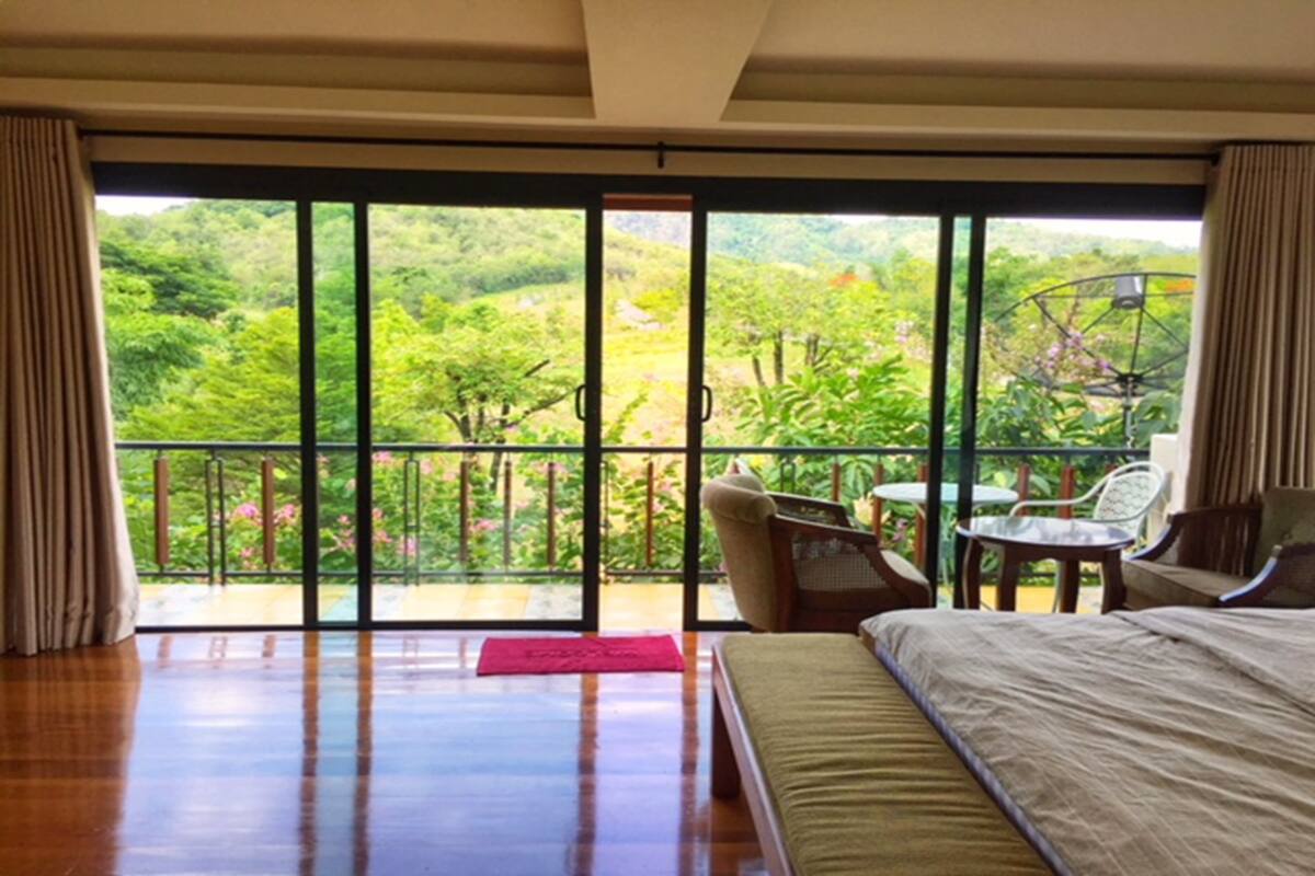 A bedroom with a large sliding glass door leading to a balcony overlooking a lush garden.