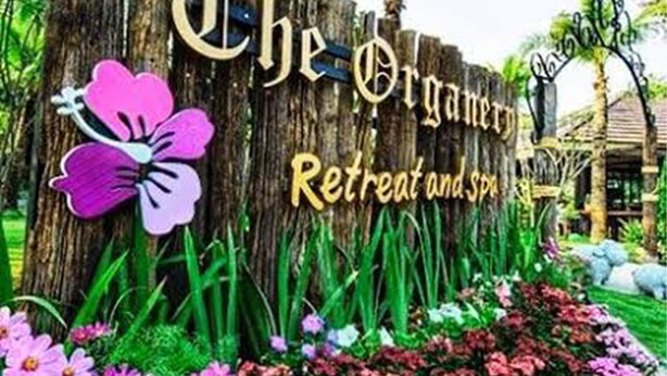 A wooden sign with "The Organism Retreat and Spa" written on it, surrounded by flowers and greenery. - The Organery Retreat (Muak Lek)