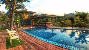 A modern pool area with a wooden deck, lounge chairs, and a covered seating area. - The Organery Retreat (Muak Lek)