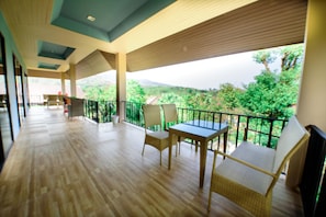 A spacious balcony with wooden flooring, wicker furniture, and a view of greenery and mountains. - The Organery Retreat (Muak Lek)