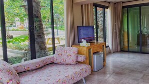A modern room with a sofa, a small table with a television, and large windows offering a view of greenery outside. - The Organery Retreat (Muak Lek)