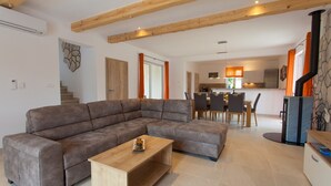 Ein modernes Wohnzimmer mit einem Ecksofa, einem Couchtisch aus Holz und einer Küche im Hintergrund.