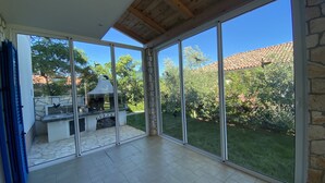 Eine geräumige Terrasse mit Kamin aus Stein und Grill, große Schiebegläser zu einem üppigen Garten.