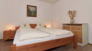 Un letto in legno con due cuscini, un comodino con una lampada, una cassettiera e un quadro appeso al muro.