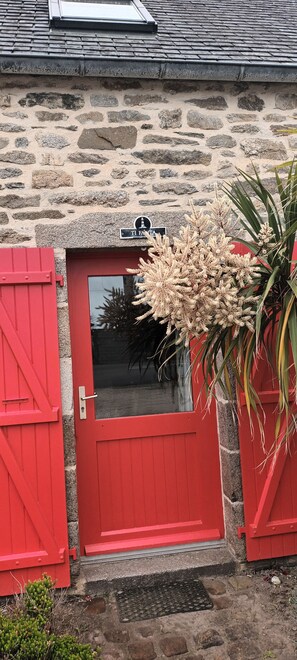 Un edificio de piedra con puerta y contraventanas rojas, una ventana pequeña y un letrero sobre la puerta.