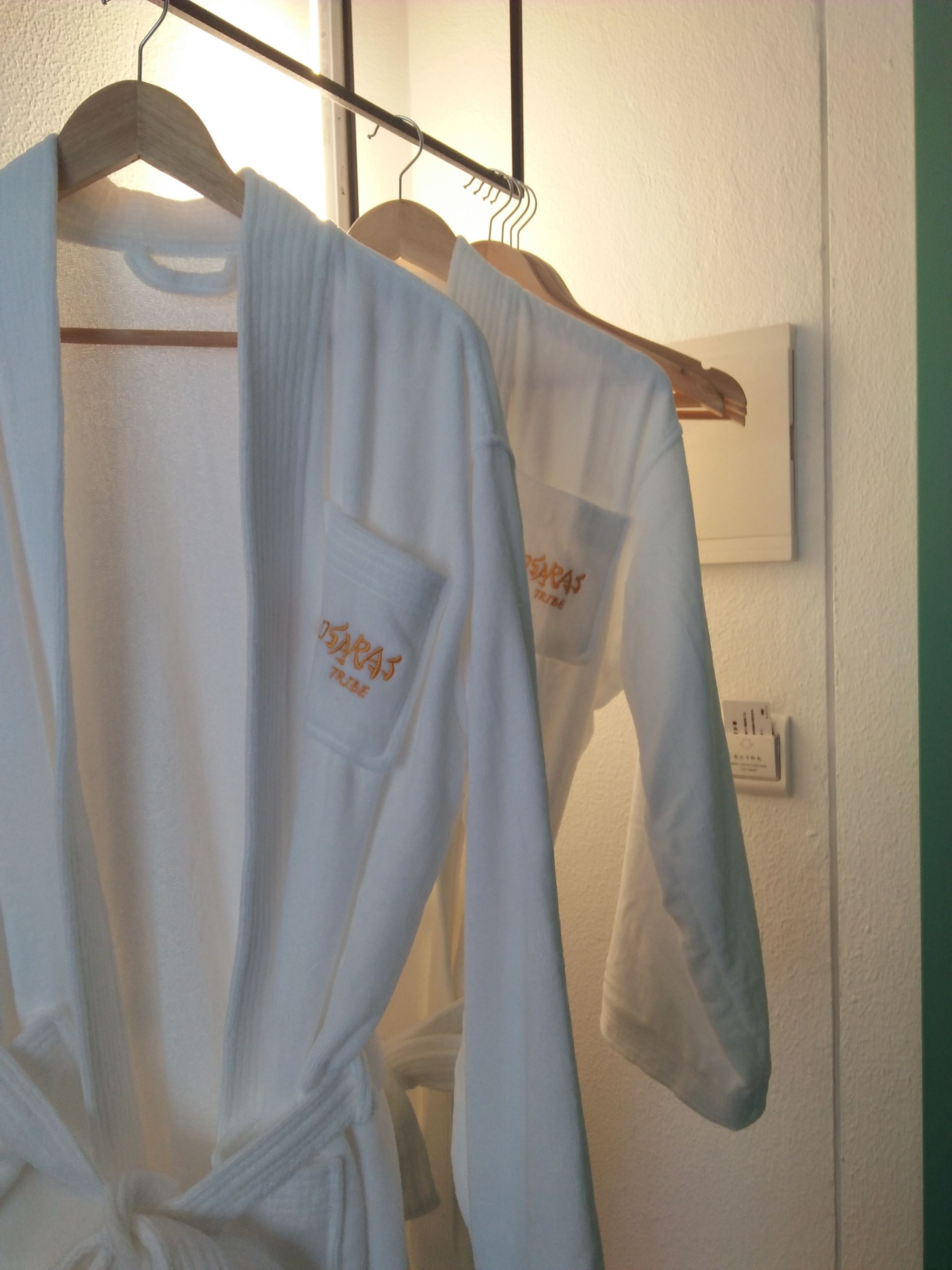 Un perchero con batas blancas con detalles bordados, un termostato y un interruptor de luz en la pared.