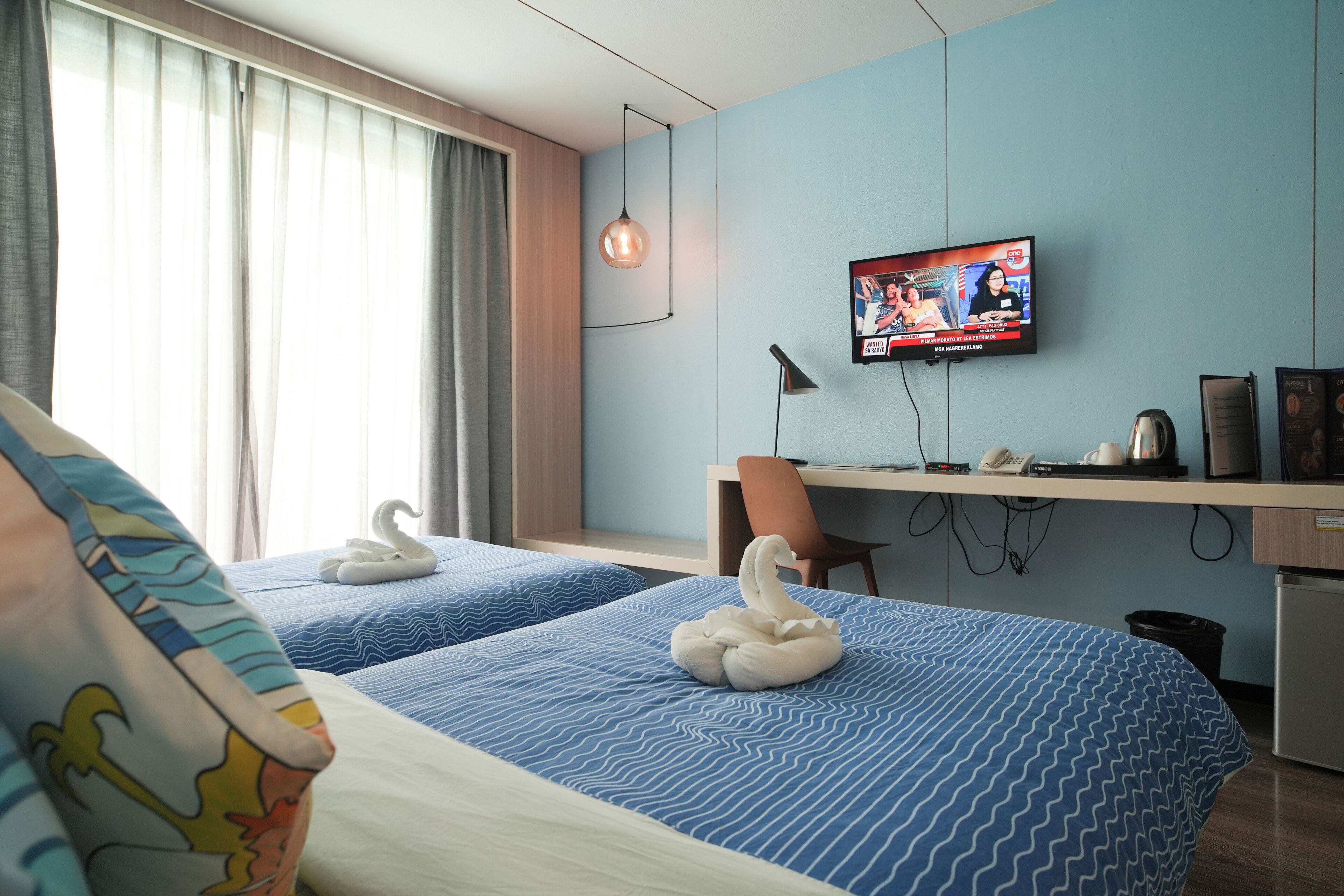 A hotel room with two beds, a desk, a TV, and a swan-shaped pillow.