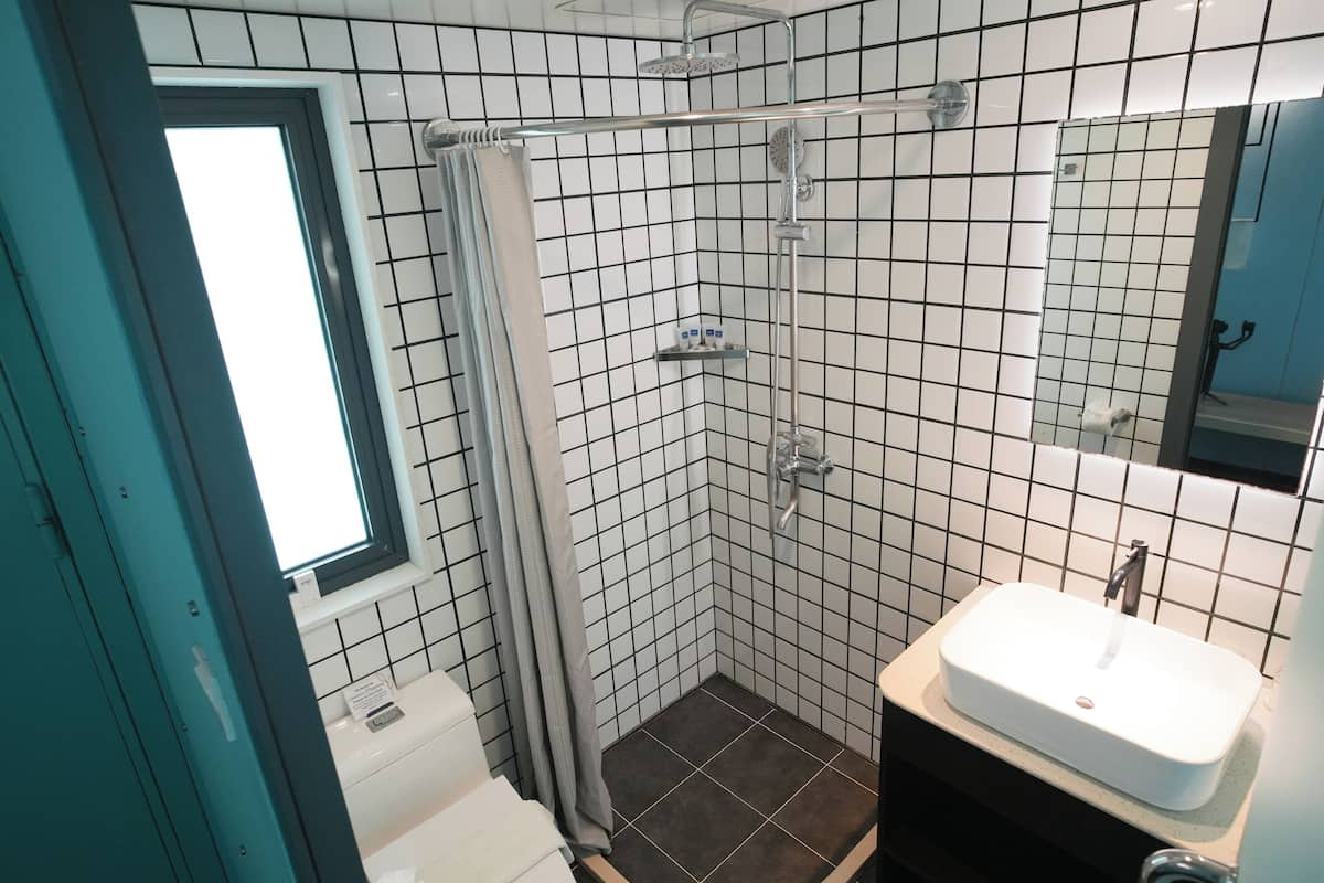 A small bathroom with a shower, a sink, and a window.