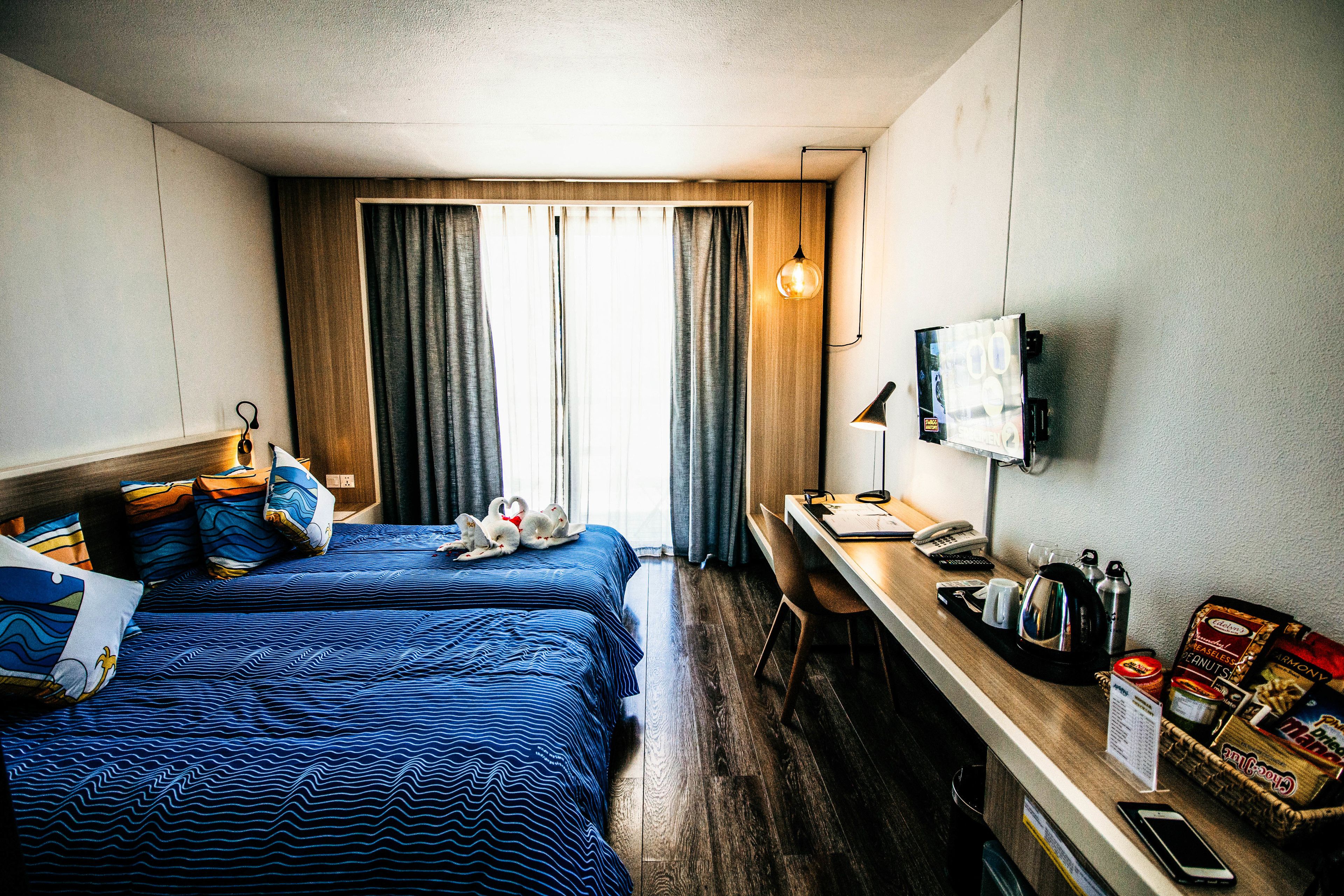 A hotel room with two beds, a desk, a TV, and a window with curtains.