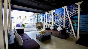 An outdoor seating area with wicker furniture, a fan, and a view of a blue building with scaffolding. - Apsaras Tribe - Siargao (General Luna)